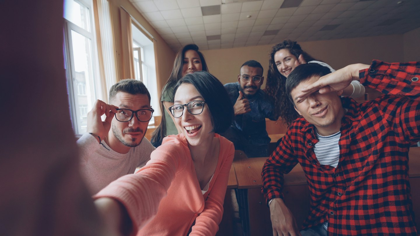 Diverse young adults taking a happy selfie in a classroom.