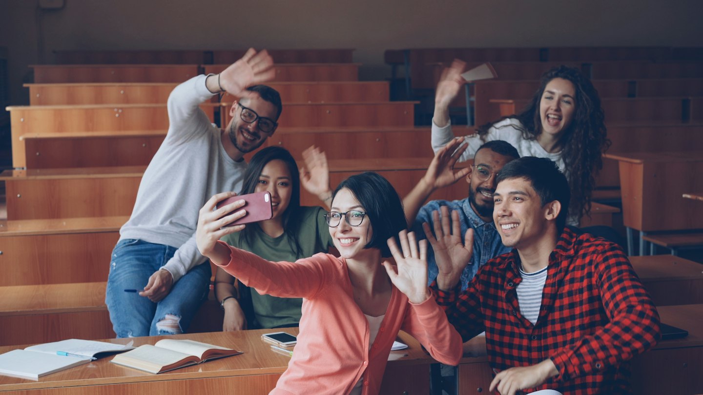 Students wave to the camera in a university lecture hall.